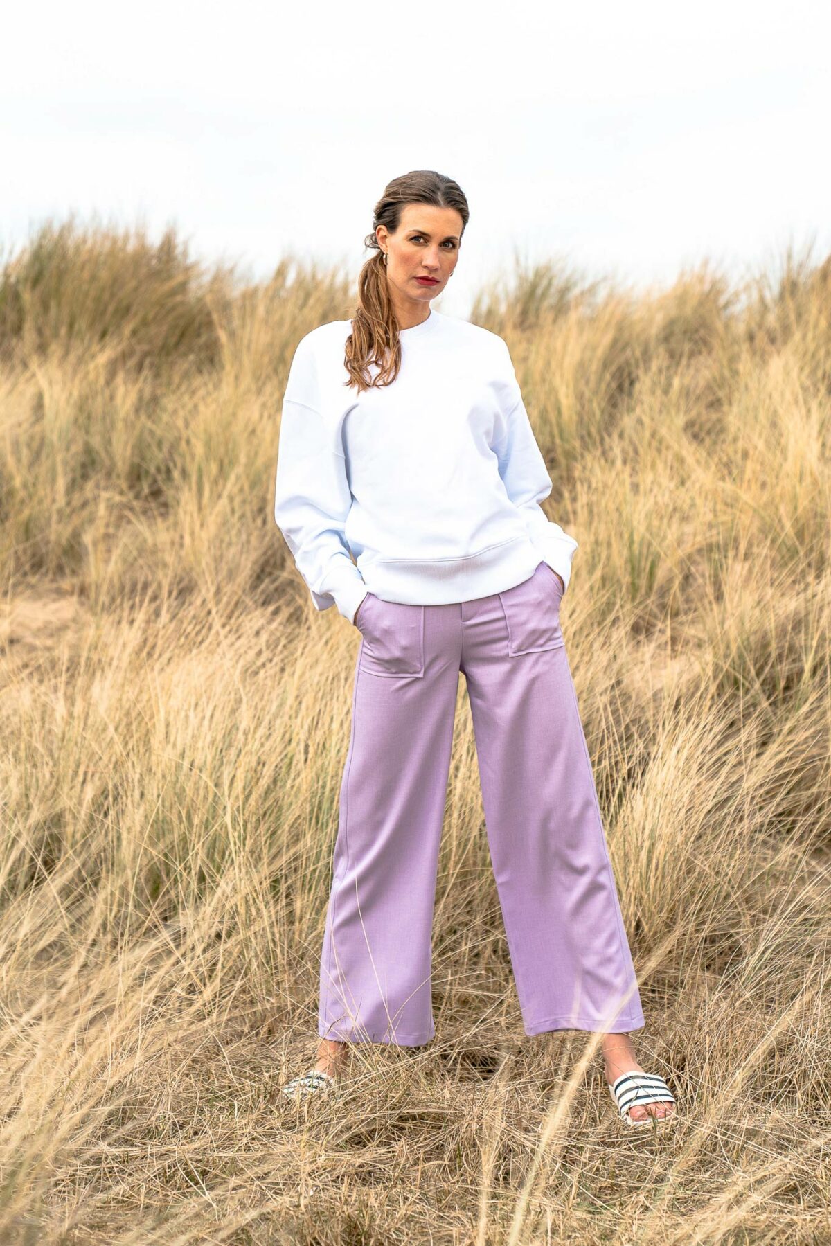 woman on the beach wearing a white sweater and lilac pants